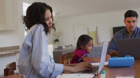 Hispanische-Eltern-Sitzen-Am-Tisch-Und-Arbeiten-Mit-Laptops-Und-Ihrer-Tochter-Zeichnen