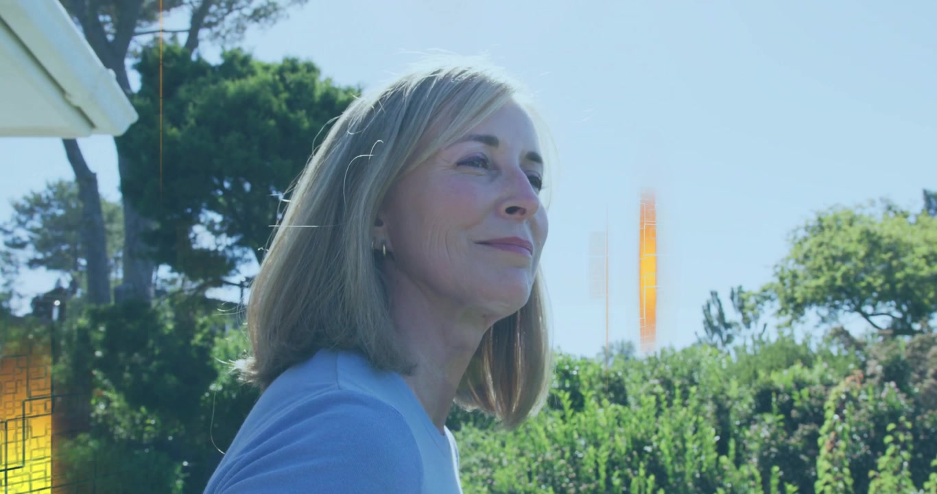 Mujer madura mirando hacia arriba en un jardín, con destellos dorados pasando por su rostro para una demostración tecnológica.
