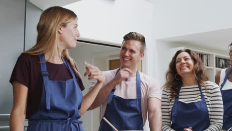 female teacher making flatbread on cooker in cookery class as adult students look on