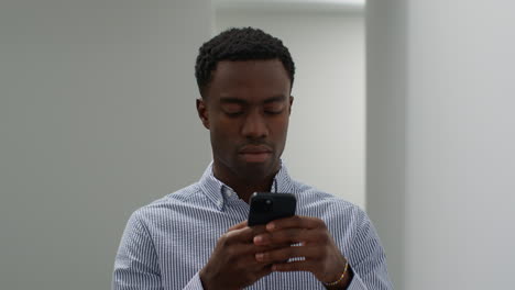 close up of young businessman walking along corridor in office towards camera messaging on mobile phone 1