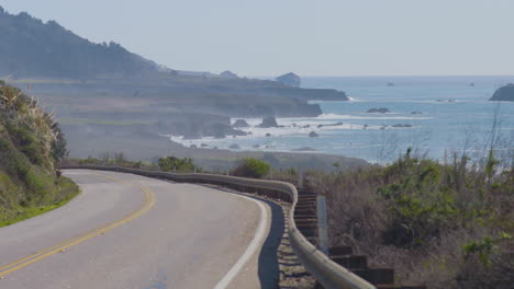 Time-lapse-of-cars-turning-navigating-around-a-bendy-road-with-the-Pacific-Ocean-waves-cashing-in-the-background-located-in-Big-Sur-California