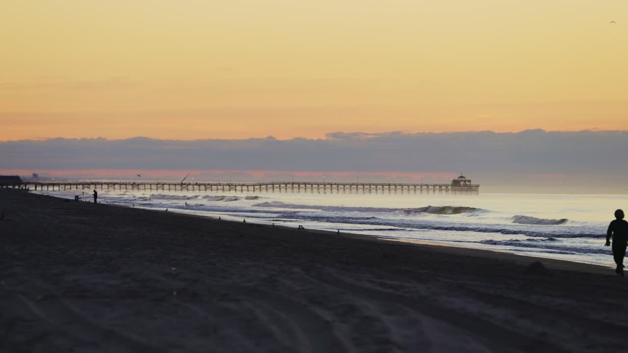 silueta de gente caminando a lo largo de north myrtle beach durante el amanecer dorado y el muelle en segundo plano