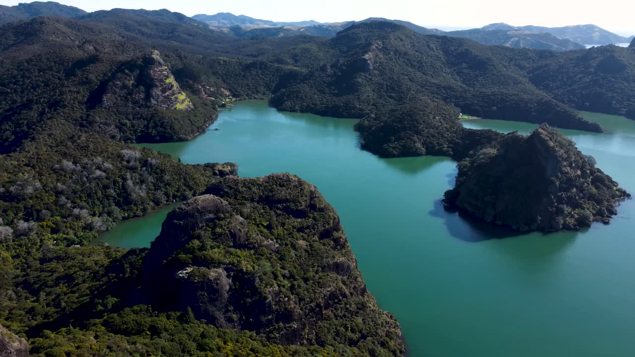 Drone view of a bay and islands with mountains, greenery and turquoise water on a sunny day in Duke's Nose, Northland, New Zealand.