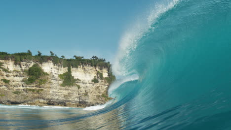 Scenic rolling wave curls toward lush tropical cliffs in golden light
