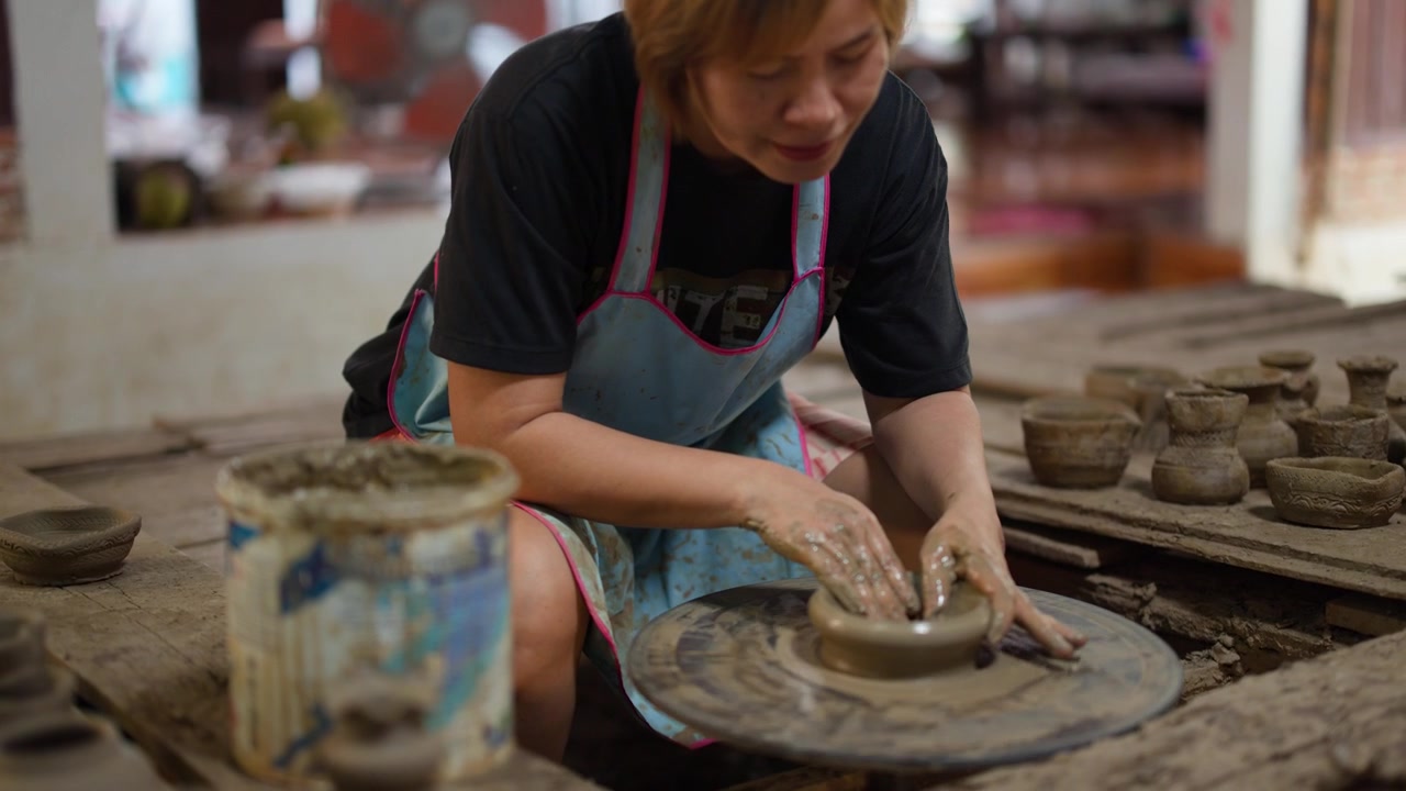 An Asian female artisan crafts traditional clay pottery on a spinning wheel in Nonthaburi.