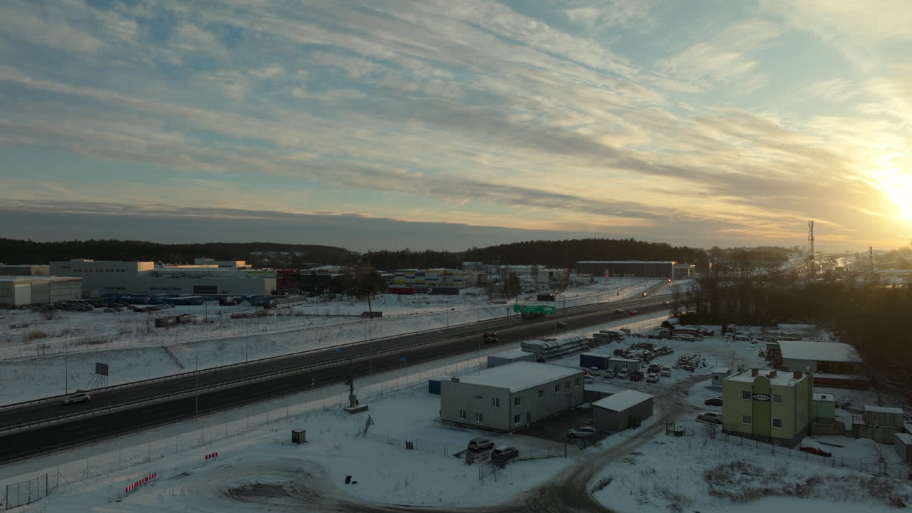 puesta de sol sobre una zona urbana cubierta de nieve con una autopista, edificios comerciales y nubes rayadas