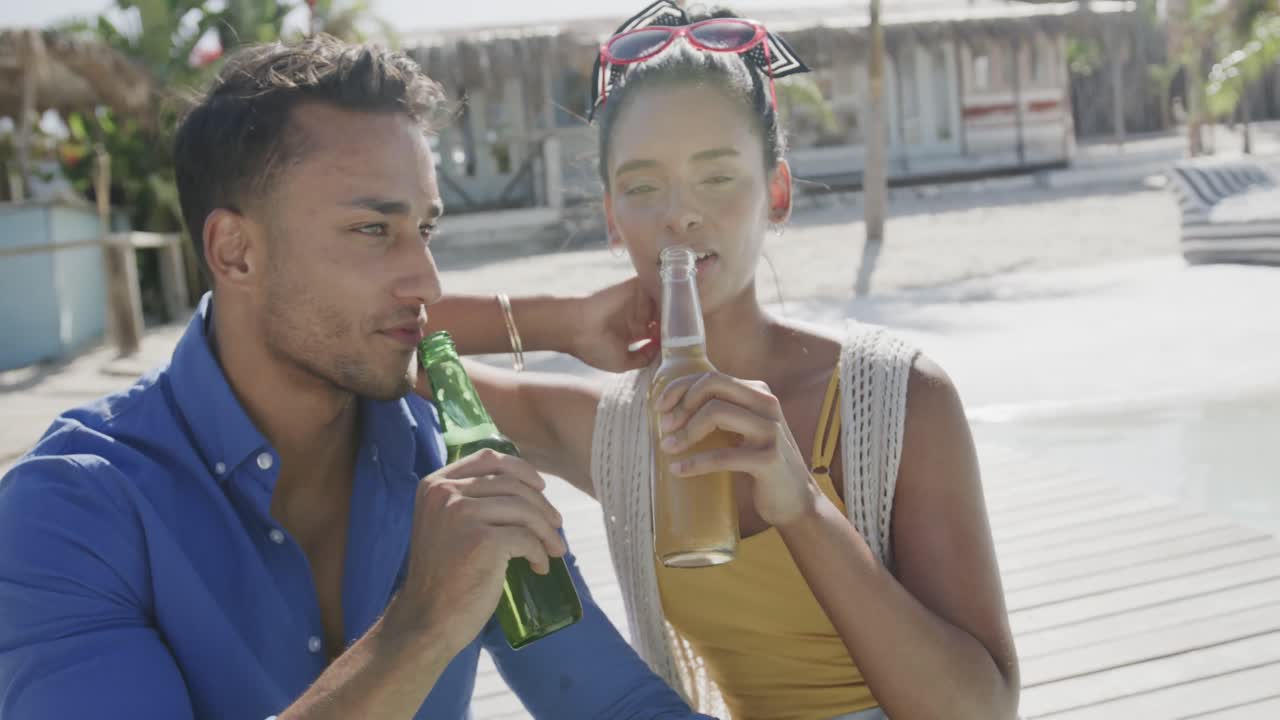pareja feliz hablando y bebiendo cervezas en la terraza del sol de la playa, en cámara lenta