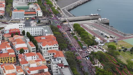 aerial orbit shot of funchal, madeira during the vibrant flower festival, capturing colorful floats, crowds, and festive atmosphere along the scenic coastal promenade