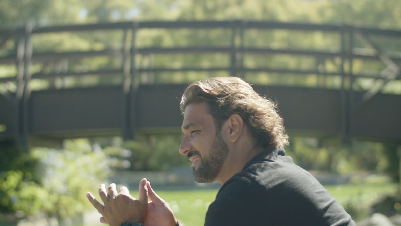 hombre pensativo frotando las palmas juntos y sentado en el parque