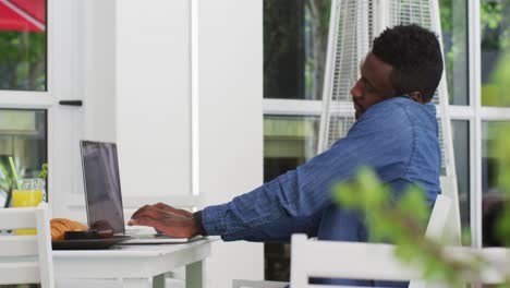 african american businessman using laptop and talking on smartphone in cafe