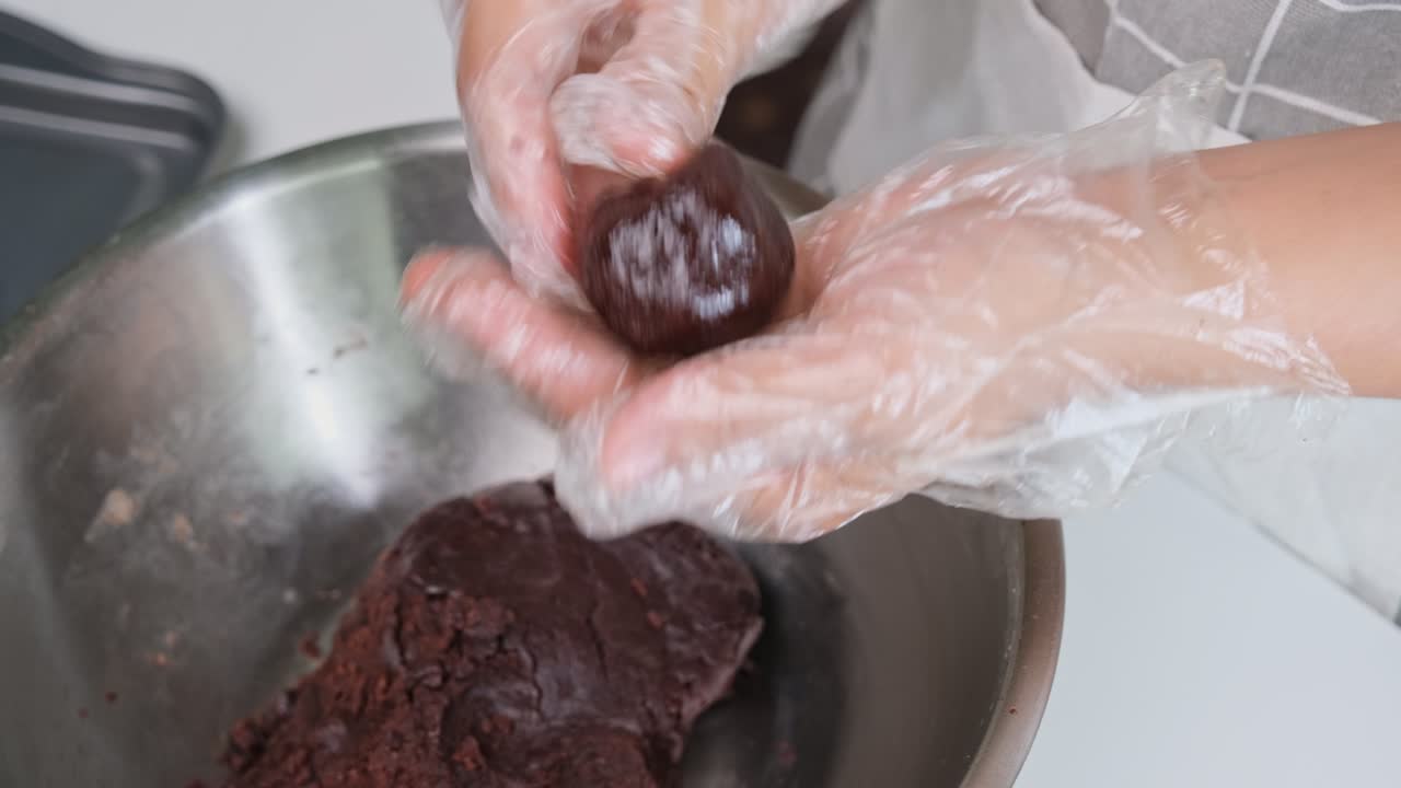 manos con guantes desechables están haciendo bolas de cacao caseras rellenas con cubos de chocolate oscuro y colocándolas en una bandeja.