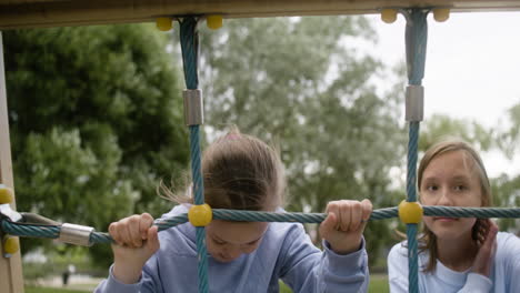 Little girl with down syndrome playing with her blonde friend in the net of a children&#039;s park on a windy day