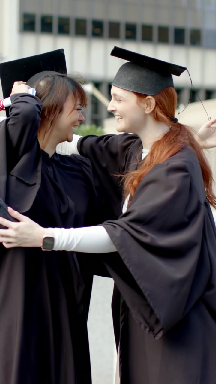 Video verticale: Ricevere diplomi, laureati che indossano toche, sistemano i cappelli e si abbracciano nel campus.