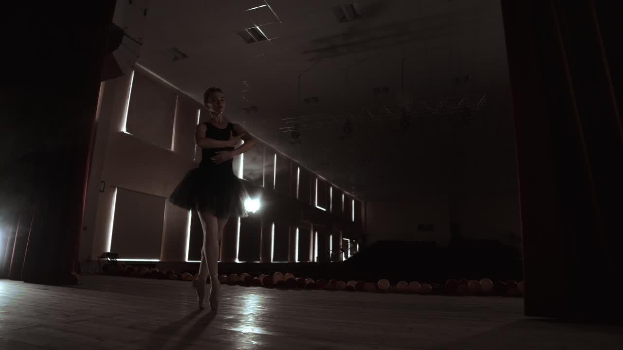 Young professional ballerina making circular movements on stage. Beautiful girl dancing in spotlights in evening during dress rehearsal