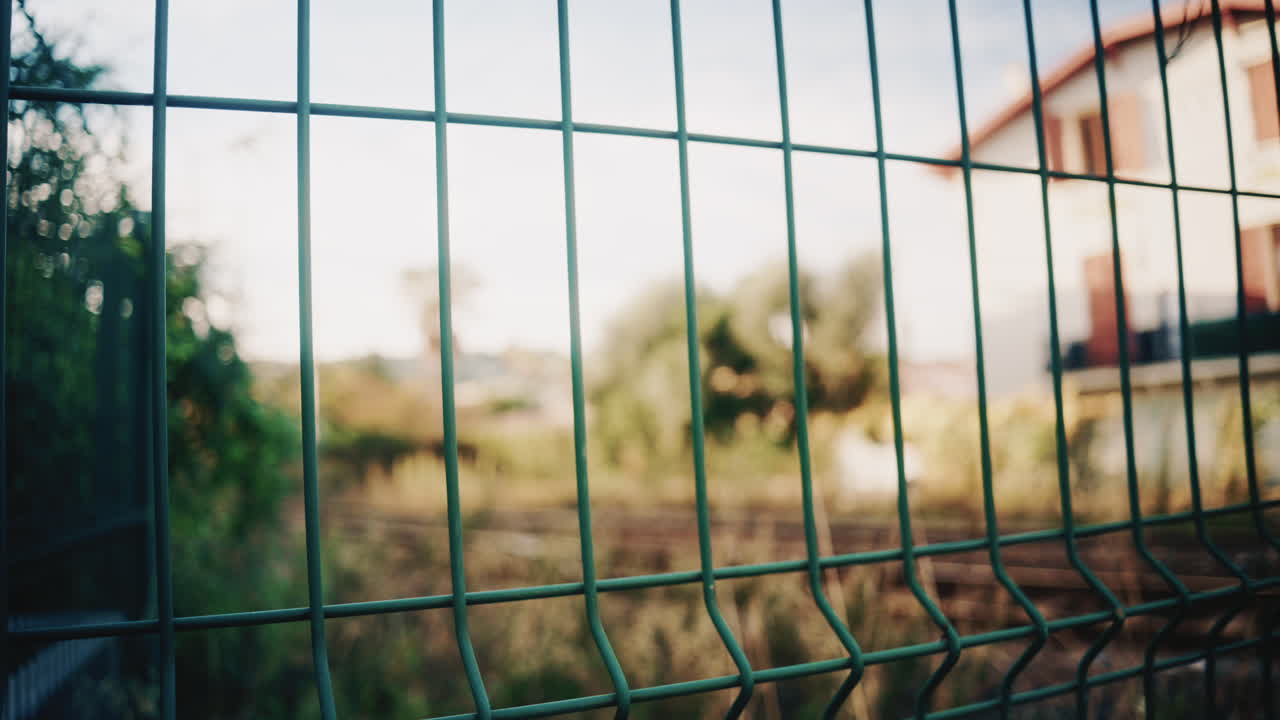 Blurry train passes behind a green metal fence, creating a layered perspective focused on the fence in the foreground