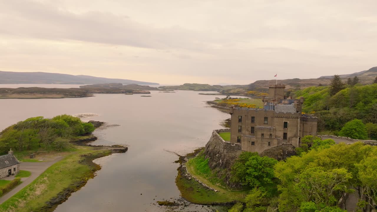Aerial drone shot of Dunvegan Castle on the Isle of Skye, Scotland, with a scenic bay in the background, surrounded by lush greenery and rugged coastal beauty