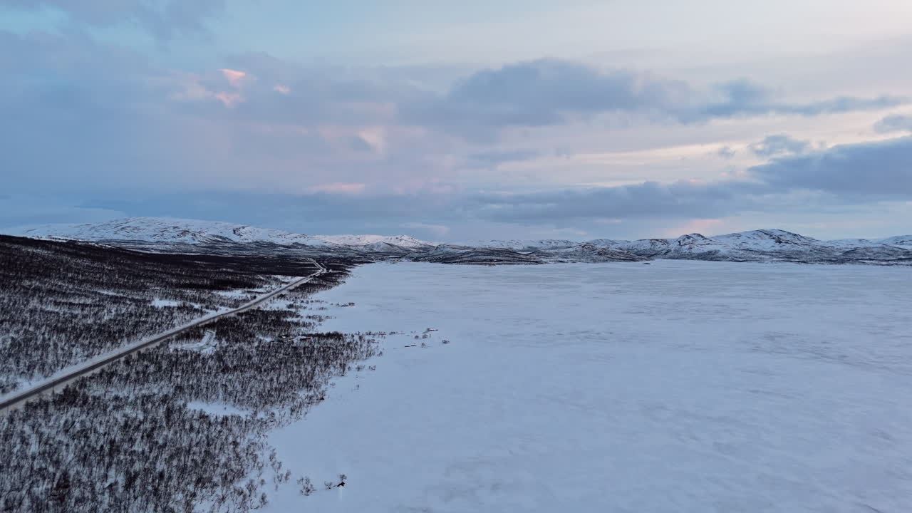 Snowy landscape of Kilpisjärvi with vast frozen lake, road, and distant mountains