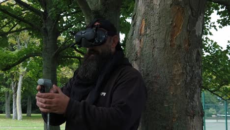 bearded male wearing fpv goggles controlling drone in park with motion controller joystick