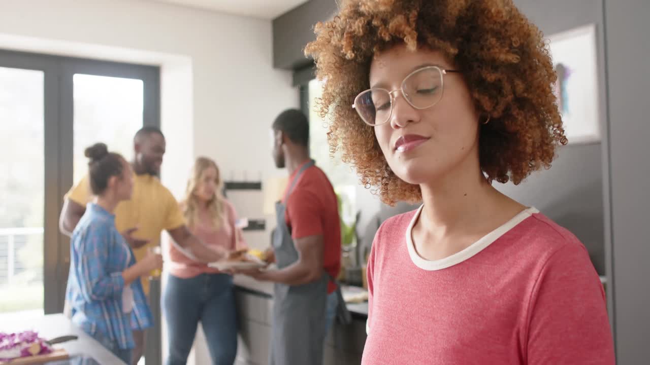 Retrato de mulher birracial feliz preparando uma refeição com amigos diversos na cozinha, em câmera lenta.