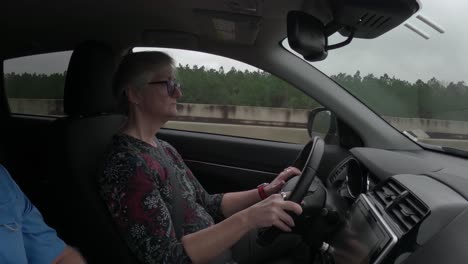 attractive mature woman singing as she drives along a highway on a road trip - interior car view