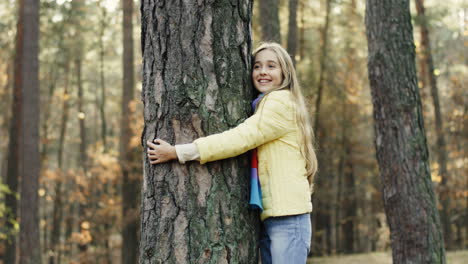 side view of a cute teen girl hugging a tree trunk with eyes closed in the forest