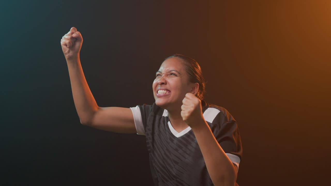 Donna afroamericana che esulta e alza i pugni in studio dopo una vittoria, indossando una maglia sportiva