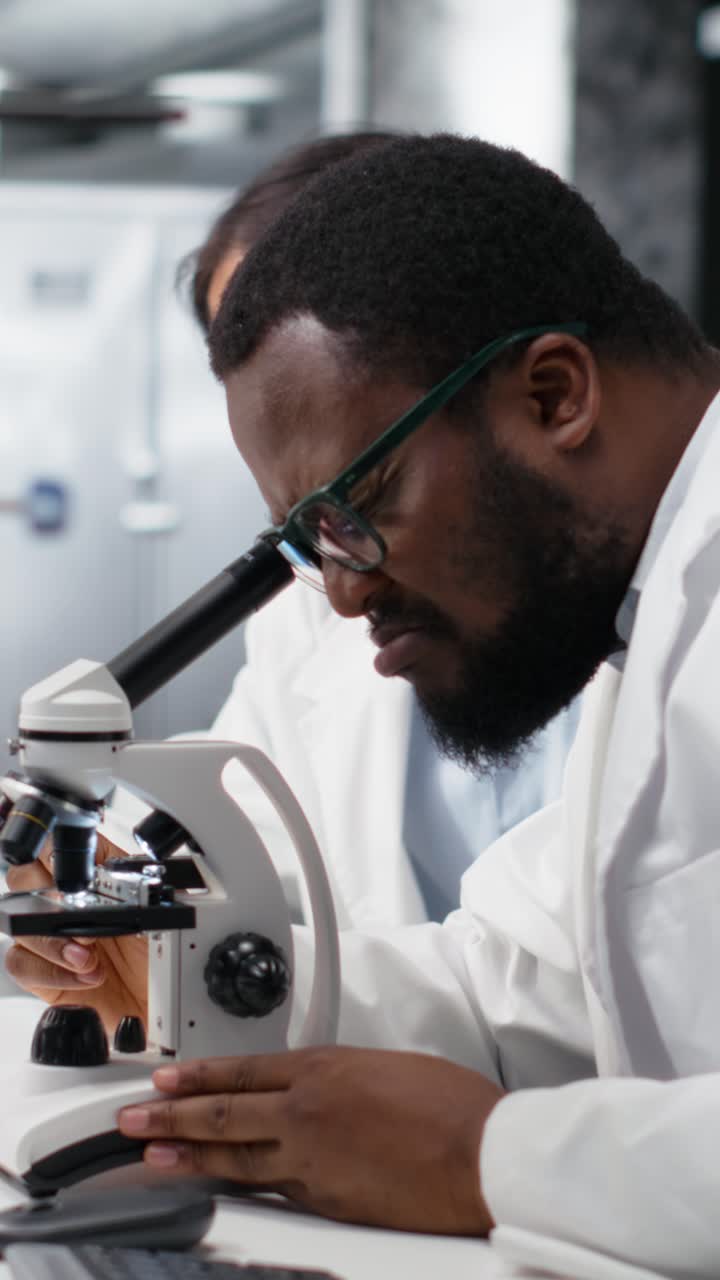 Vertical video Clinical microbiologists using microscope to evaluate cellular structures