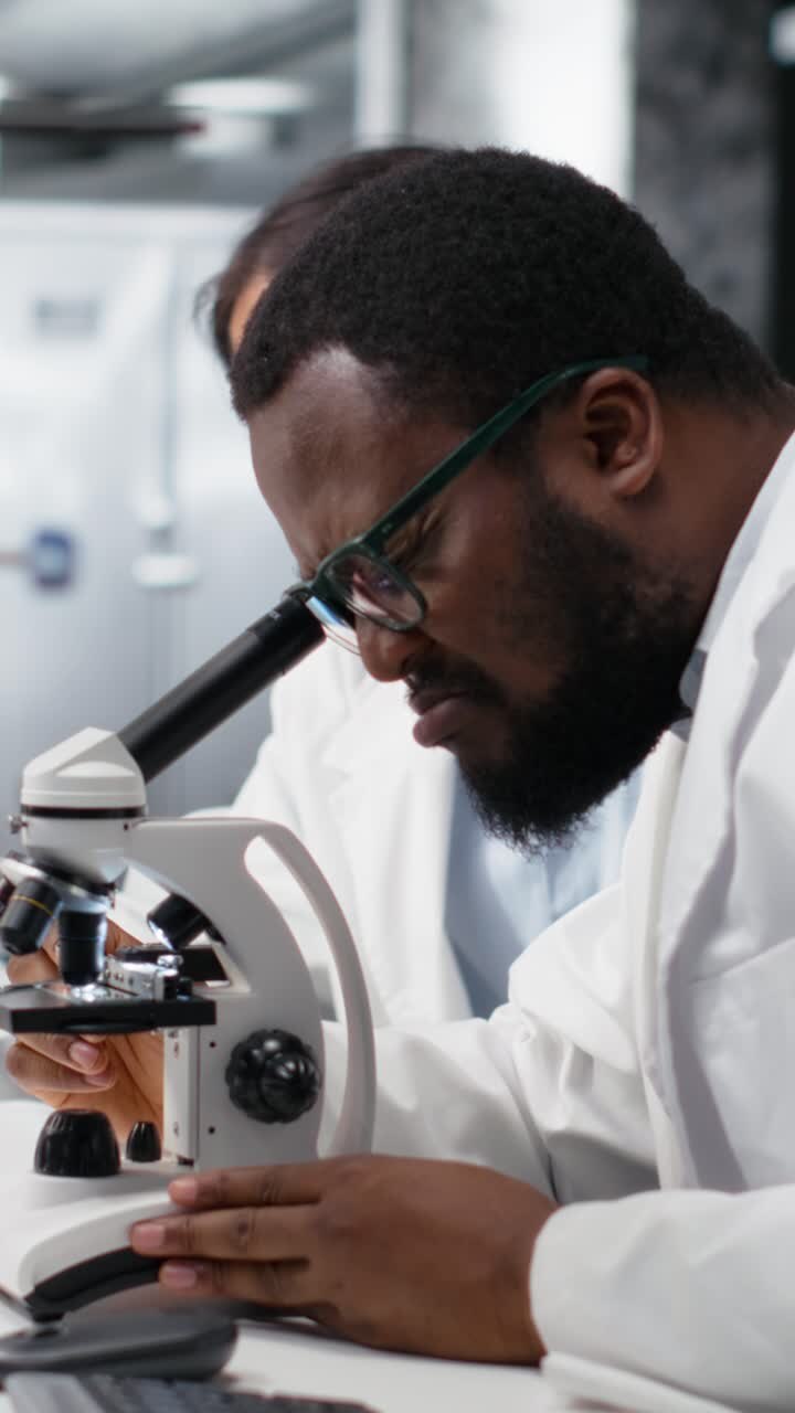Vertical video Clinical microbiologists using microscope to evaluate cellular structures