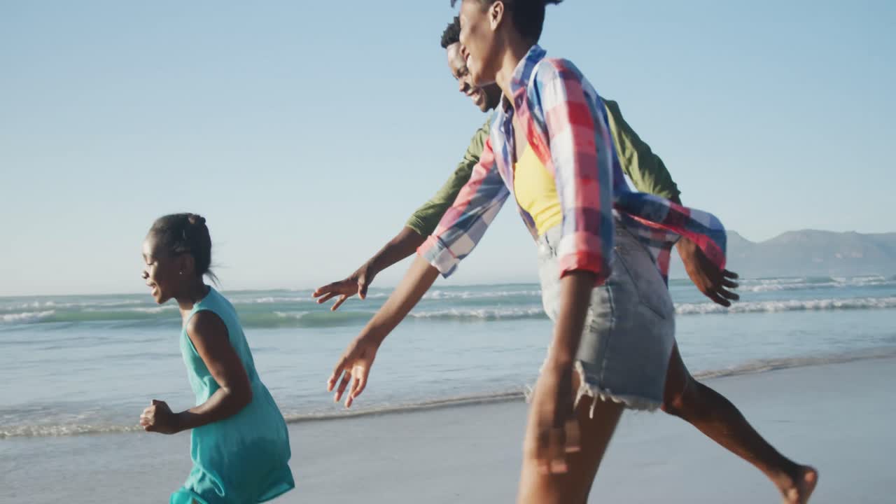 Happy african american couple running with daughter on sunny beach