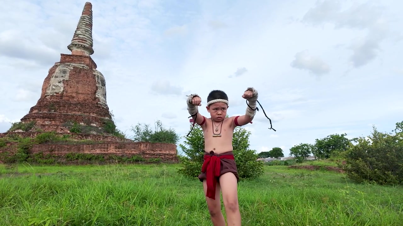 Một đứa trẻ châu Á trong trang phục truyền thống thực hiện các động tác võ thuật tại một di tích đền thờ lịch sử.