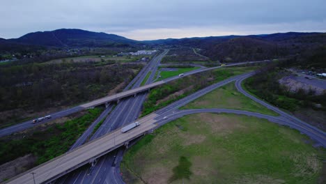 Drone-view-of-I-80-highway-interchange-with-lush-green-surroundings-under-a-cloudy-sky,-showcasing-connectivity-in-Pennsylvania