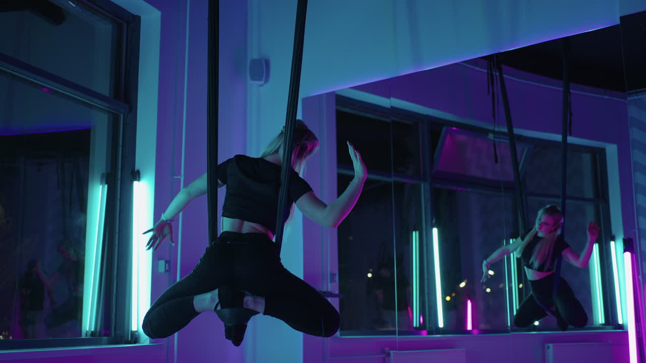 una mujer está meditando en una hamaca practicando fly-yoga en clase de fitness mirándose en el espejo.