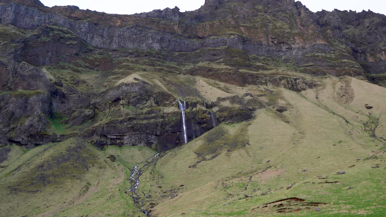 lado de montaña verde con una cascada en islandia, que muestra la tranquilidad de la naturaleza