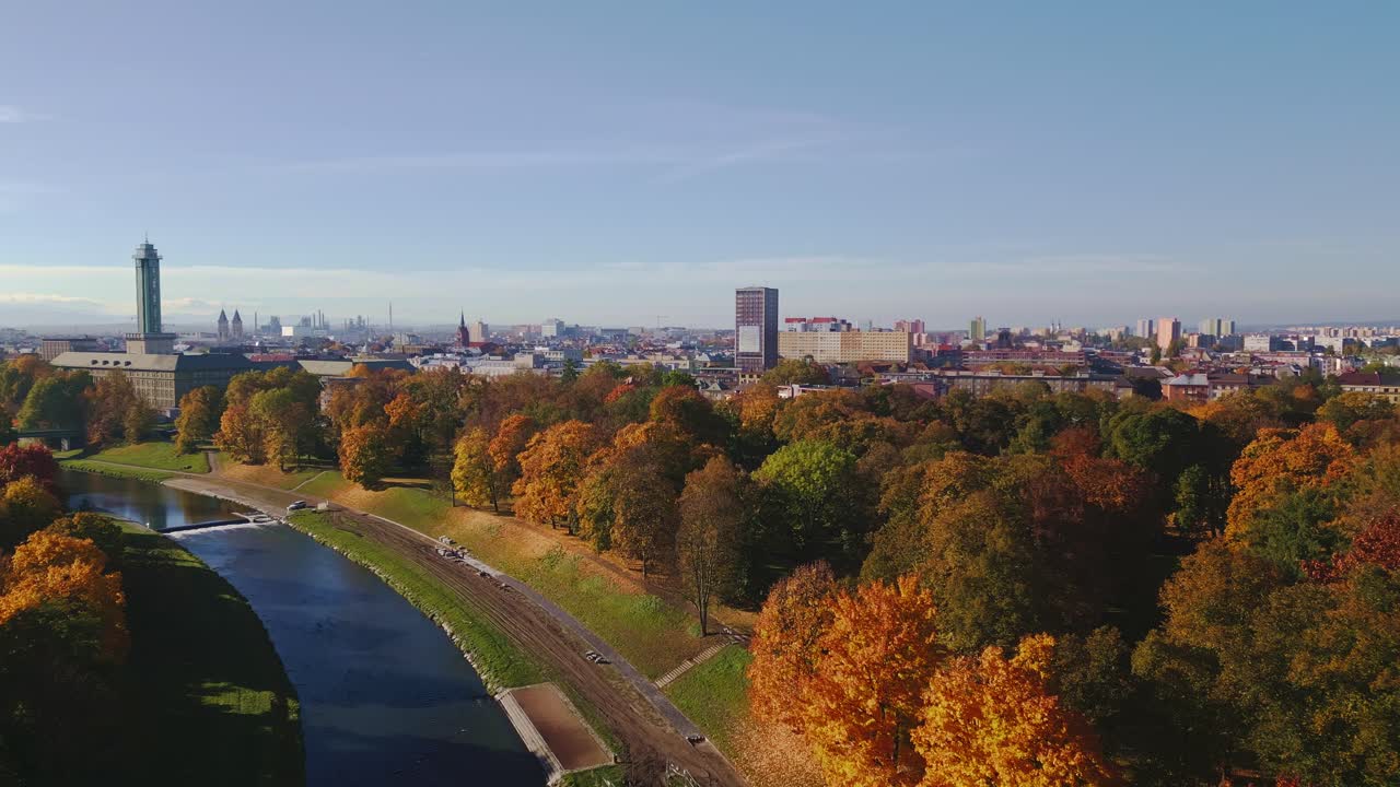 Golden autumn trees along River Ostravice with city backdrop AERIAL