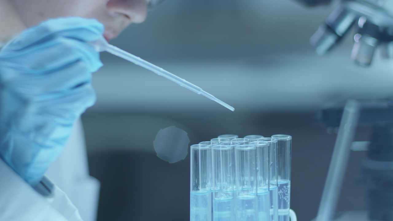 Female Microbiologist Pouring Liquids in Test Tubes with Pipette in Laboratory