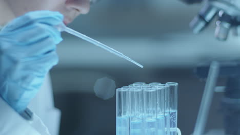 female microbiologist pouring liquids in test tubes with pipette in laboratory
