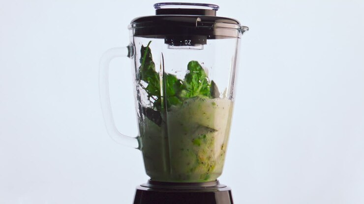 Electric blender mixing vegetable fruits herbs in super slow motion close up.