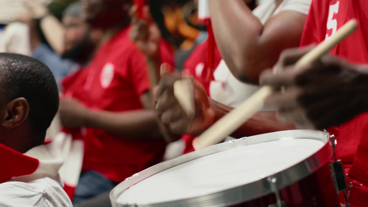 Close up of soccer supporter using drum to unite red fan section in stadium