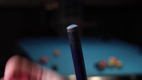 putting chalk on a pool cue to have better grip with game of pool billiards in the background