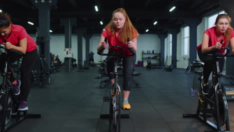 Grupo-De-Mujeres-Atléticas-Montando-En-Rutina-De-Entrenamiento-De-Bicicleta-Estacionaria-Giratoria-En-El-Gimnasio,-Pérdida-De-Peso-En-Interiores