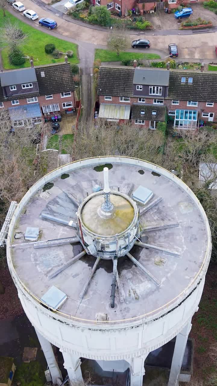 Drone-tilbagetrækning fra Bengeo vandtårn, oppefra, kamera låst på tag og telekommunikationsmast, derefter udvides billedet for at afsløre omkringliggende huse, veje og træer i Hertford, England