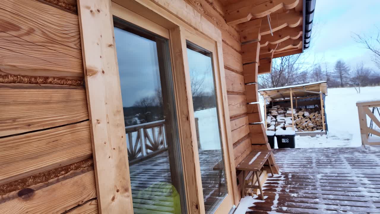 Scena invernale e tranquilla della terrazza di una baita in legno, mentre la camera si sposta oltre una panchina gelida verso le cime innevate in lontananza
