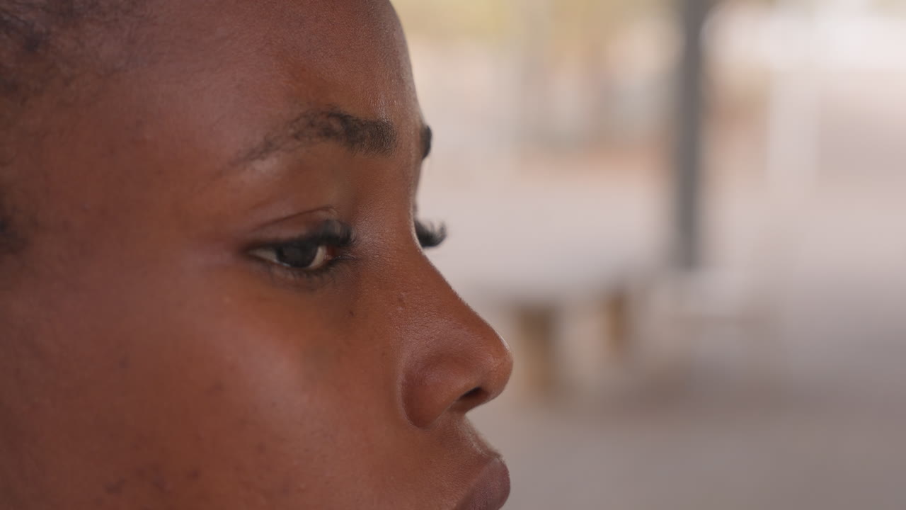 Portrett fanger den ettertenksomme stemningen hos en svart student i myk belysning. Visuell fremstilling av svart student som viser introspeksjon med detaljerte hud- og øyeteksturer i utendørs miljø.