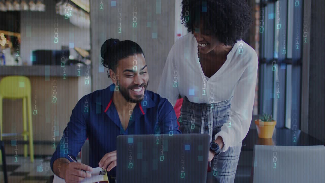 Woman leaning over laptop pointing, man smiling, writing, data symbols appearing during tech review