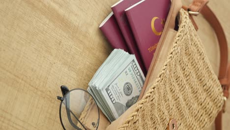 Money, Passports, and Glasses in a Straw Bag on a Wooden Surface