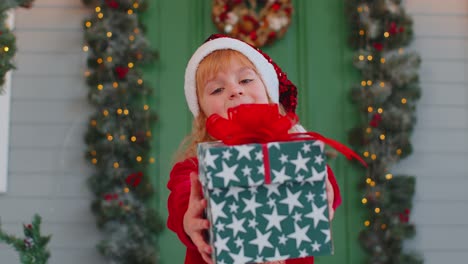 happy toddler child girl kid in red sweater gifting one christmas present box, stretches out hands