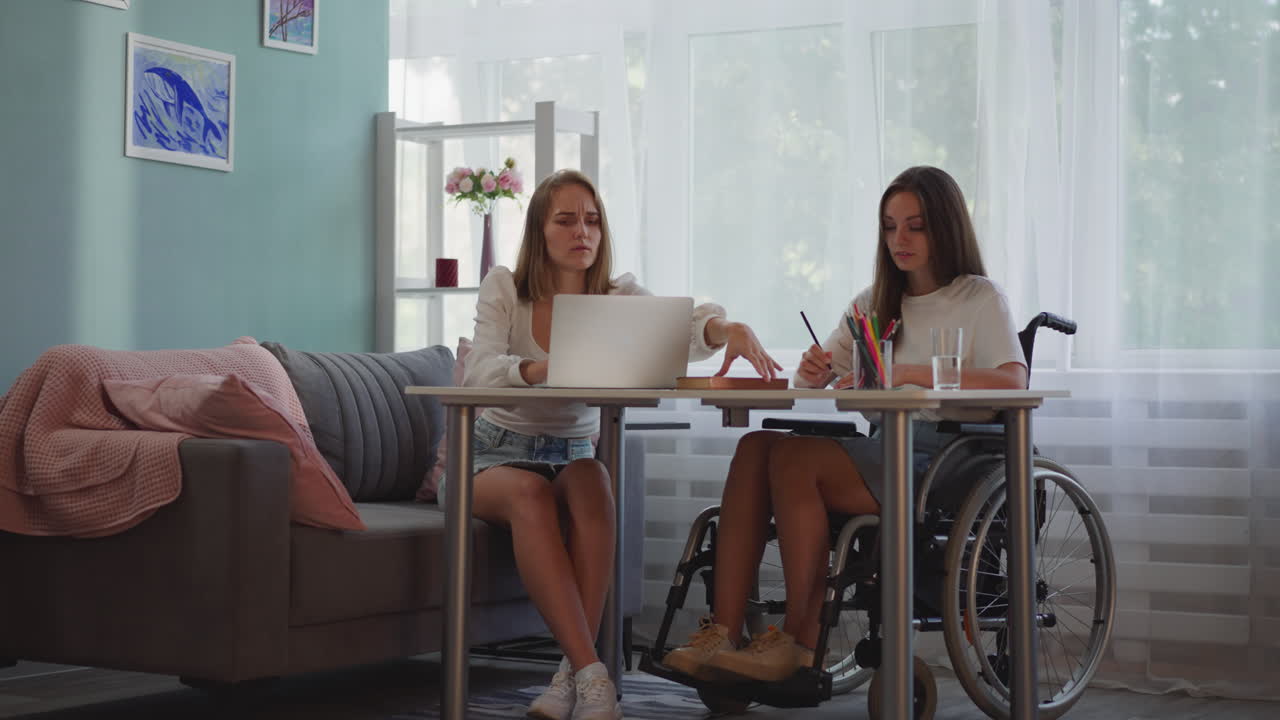 장애가 있는 여성은 노트북을 사용하는 금발 친구와 함께 메모를 합니다.