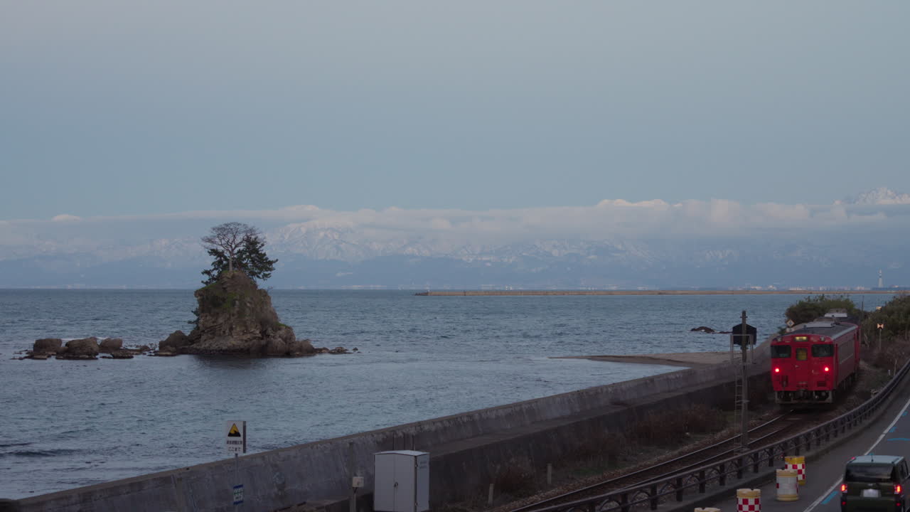 A red train is moving along the coastline of Amaharashi, Toyama, Japan
