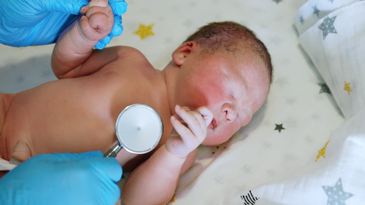 Doctor in gloves listening a baby with stethoscope. Naked newborn baby waving hands. Top view close up.