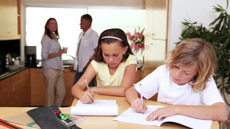 Brother-and-sister-doing-homework-in-the-kitchen-with-parents-behind-them